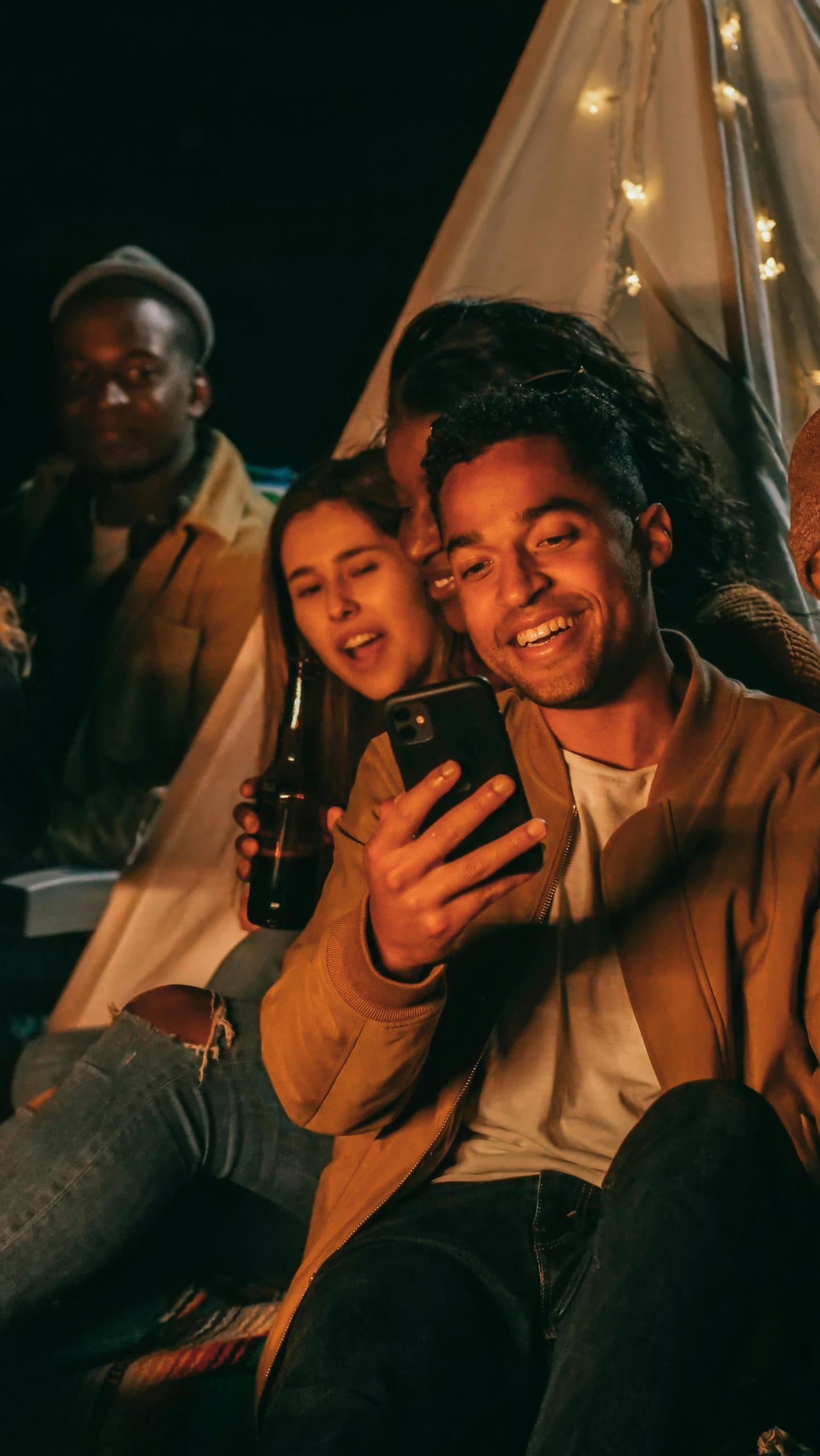 A group of friends socializing around a tent at night, enjoying each other's company.
